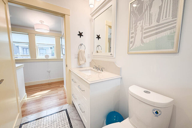 Bathroom with white vanity, marble countertop, and framed art, opening to a hardwood-floored room. - 3752 West 23rd Avenue, Vancouver West Side