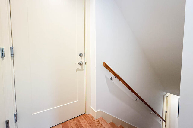 Stair landing with a white paneled door, hardwood floors, and a wooden handrail descending the steps. - 3752 West 23rd Avenue, Vancouver West Side
