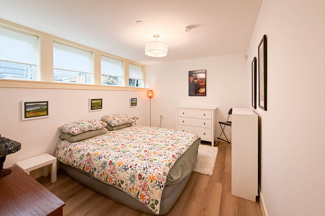 Furnished bedroom with floral bedding, hardwood floors, and a row of bright windows. - 3752 West 23rd Avenue, Vancouver West Side