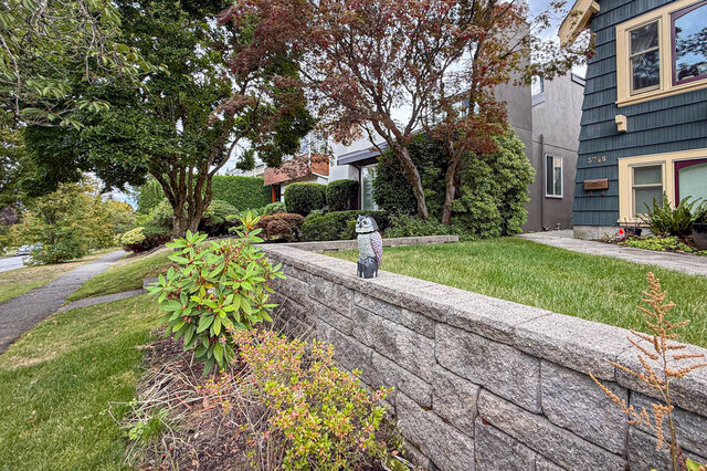 Landscaped yard with a stone retaining wall, manicured lawn, and a decorative owl statue among mature trees.