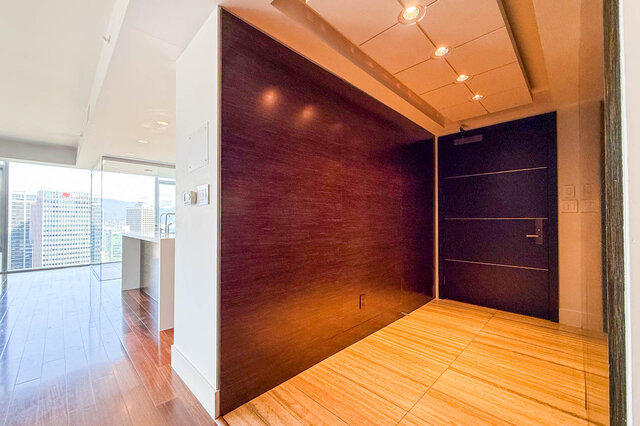 Modern entryway with dark wood paneling and light tile flooring, opening to a living room with city views. - 2702-667 Howe Street, Vancouver Downtown
