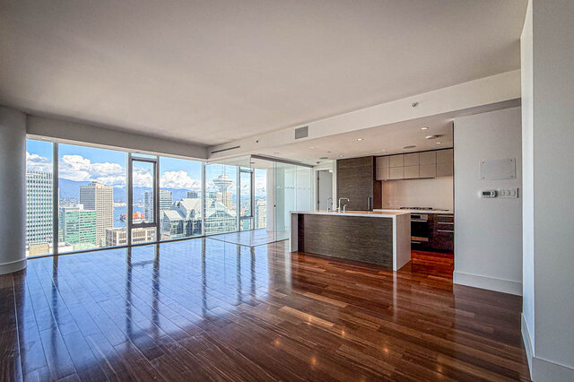 Open-concept living and kitchen with dark hardwood floors, a stone island, and floor-to-ceiling windows with city views.