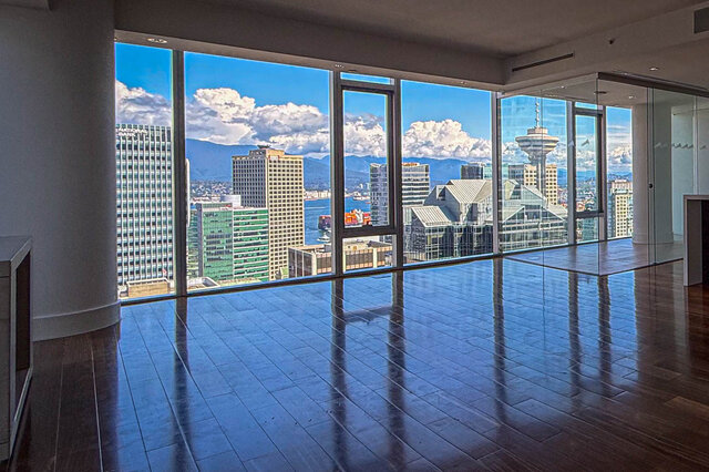 Spacious living room with dark hardwood floors and floor-to-ceiling windows framing a panoramic Vancouver city view.