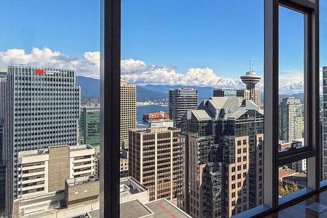 Living room with floor-to-ceiling windows framing a panoramic downtown Vancouver skyline and distant mountains.