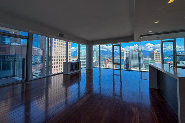 Spacious living room with dark hardwood floors and floor-to-ceiling windows framing a panoramic city and mountain view.