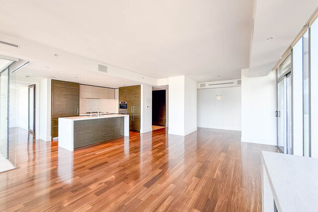 Open kitchen and living area with polished hardwood floors, a white-topped island, and floor-to-ceiling windows.