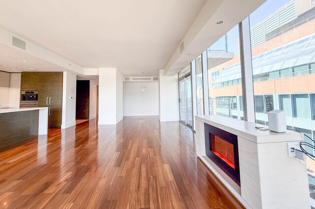 Spacious living room with glossy hardwood floors, a modern fireplace, and floor-to-ceiling windows offering a city view.