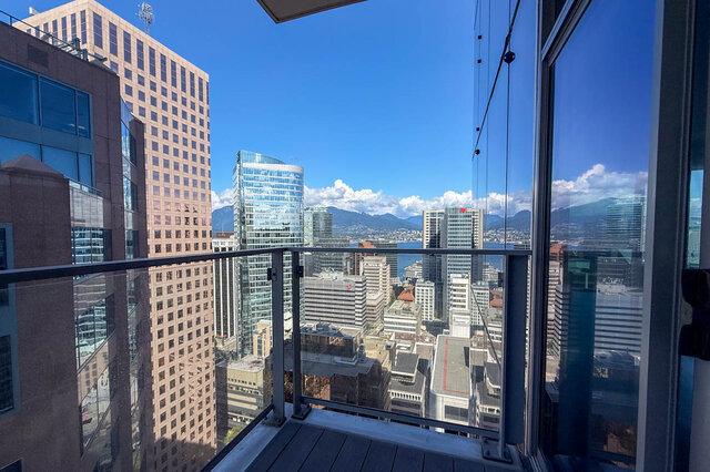Spacious balcony with glass railing and wooden deck overlooking a panoramic downtown skyline and distant mountains.