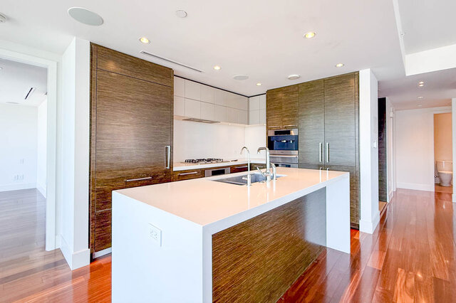 Modern kitchen featuring a white island, wood-grain cabinetry, and glossy hardwood floors. - 2702-667 Howe Street, Vancouver Downtown