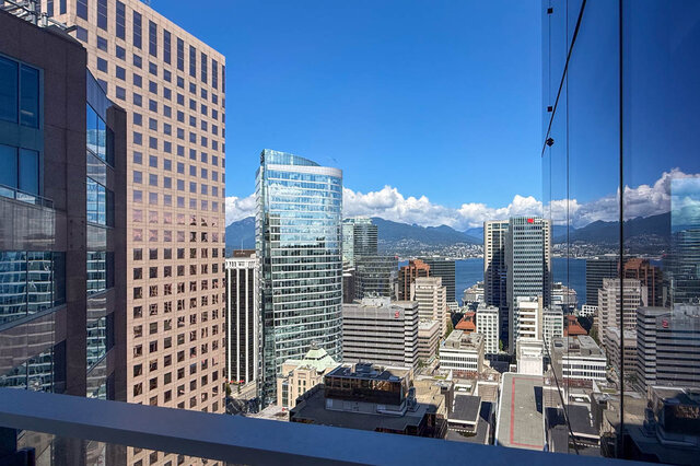 Balcony with glass railing offering a sweeping downtown skyline view of high-rises, water, and mountains. - 2702-667 Howe Street, Vancouver Downtown