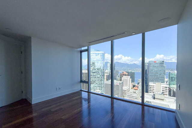 Spacious living room with dark hardwood floors and floor-to-ceiling windows framing a downtown city and mountain view.