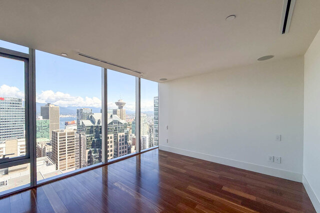 Spacious living room with dark hardwood floors and floor-to-ceiling windows framing a panoramic downtown city view.