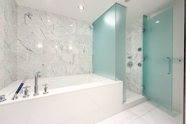 Modern bathroom with white marble tile walls, a built-in soaking tub, and a frosted glass shower enclosure. - 2702-667 Howe Street, Vancouver Downtown