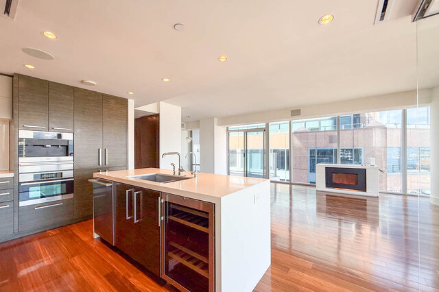 Modern kitchen with white island countertops, dark wood cabinetry, and floor-to-ceiling windows overlooking the city.