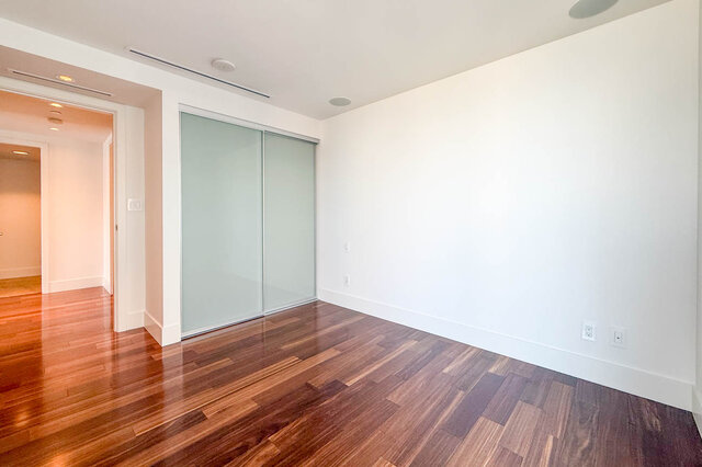 Empty bedroom with polished hardwood floors and frosted glass sliding closet doors. - 2702-667 Howe Street, Vancouver Downtown