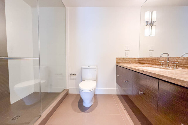 Modern bathroom with dark wood vanity, stone countertop, and glass-enclosed shower. - 2702-667 Howe Street, Vancouver Downtown
