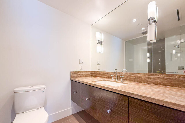 Modern bathroom with a wood vanity, beige stone countertop, undermount sink, and large frameless mirror. - 2702-667 Howe Street, Vancouver Downtown