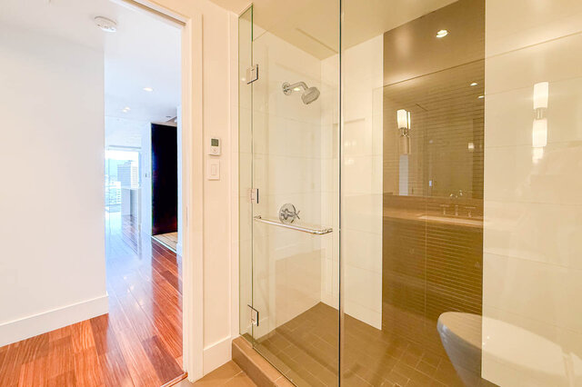 Modern bathroom with a glass-enclosed walk-in shower, white tile, and hardwood floors leading to a city view.