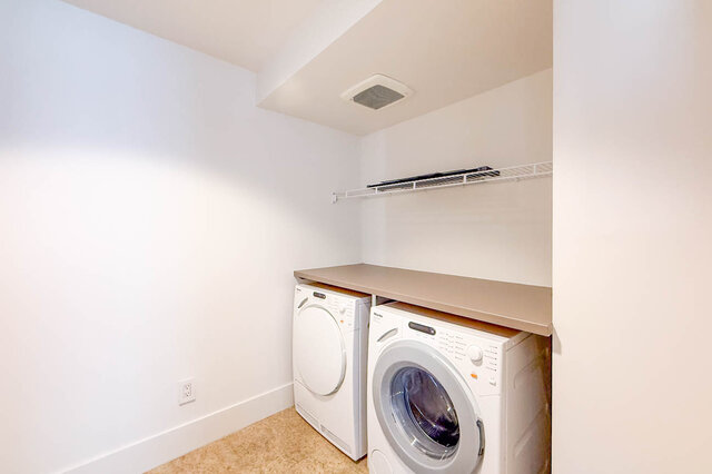 Compact laundry room with front-load washer and dryer, beige countertop, and wall-mounted wire shelving. - 2702-667 Howe Street, Vancouver Downtown