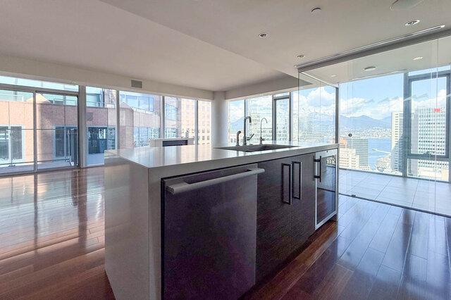 Modern kitchen island with white countertops and dark wood cabinets, framed by floor-to-ceiling windows and a city view.