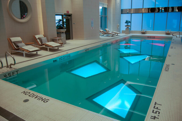 Indoor pool with turquoise water, cushioned lounge chairs, and large blue-tinted windows. - 2702-667 Howe Street, Vancouver Downtown