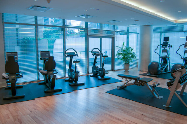 In-unit gym with hardwood floors, large windows, and a lineup of cardio machines and a weight bench. - 2702-667 Howe Street, Vancouver Downtown