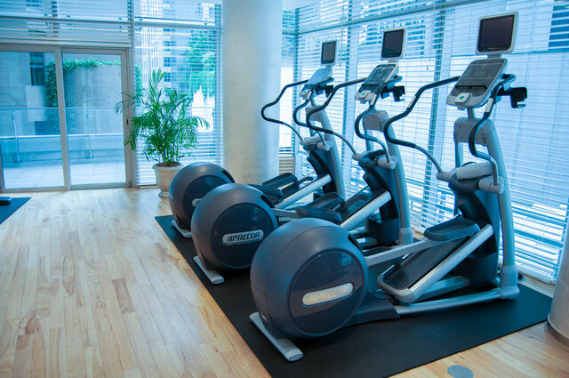 In-unit gym space with three elliptical trainers on light hardwood floors and floor-to-ceiling windows. - 2702-667 Howe Street, Vancouver Downtown