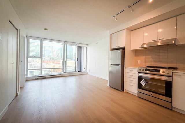 Open-concept dining and kitchen with white cabinetry, hardwood floors, and a city view through floor-to-ceiling windows.