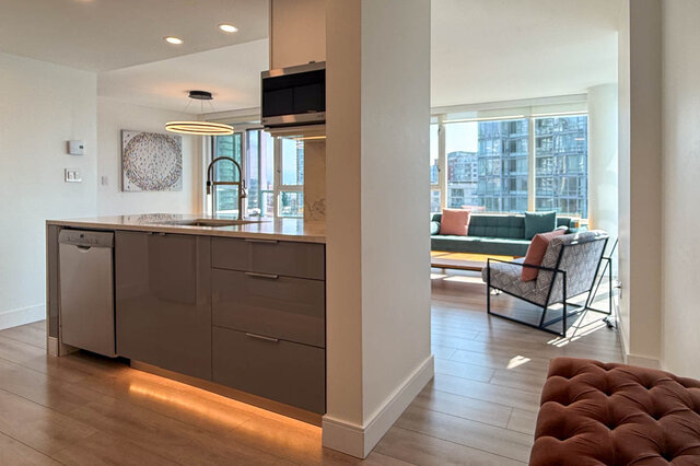 Modern kitchen island with grey cabinetry and under-cabinet lighting, opening to a living room with city views.