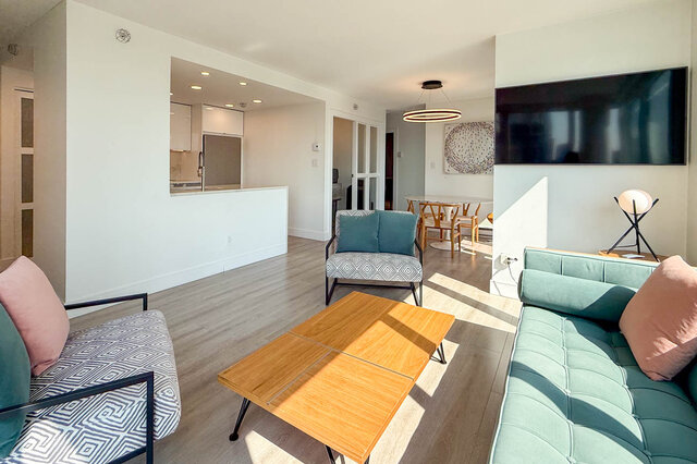 Living room with light wood floors, green tufted sofa, and open view to dining and kitchen. - 1101-1067 Marinaside Crescent, Vancouver Downtown
