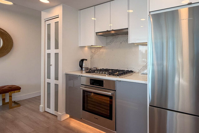 Modern kitchen with white cabinetry, stainless steel appliances, and a marble-look backsplash. - 1101-1067 Marinaside Crescent, Vancouver Downtown