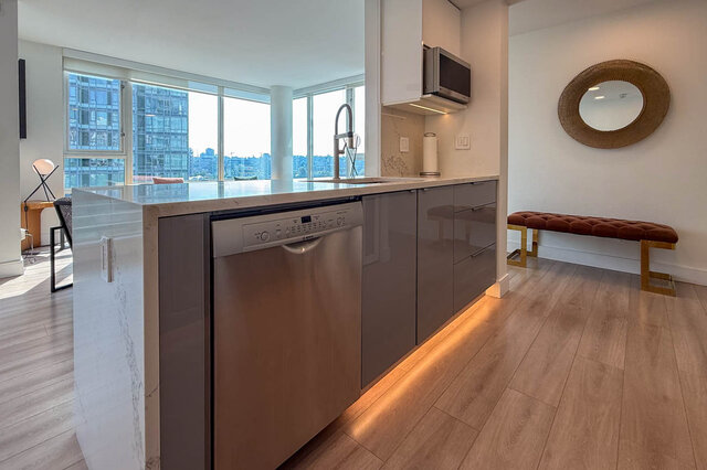 Modern kitchen with marble countertops, grey cabinetry, and floor-to-ceiling windows framing a city view.