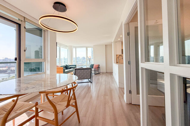 Bright dining area with a marble table, woven-wood chairs, and light hardwood floors overlooking the city.