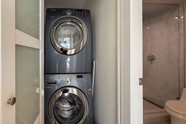 Compact laundry alcove with stacked front-load washer and dryer beside a marble-tiled shower. - 1101-1067 Marinaside Crescent, Vancouver Downtown
