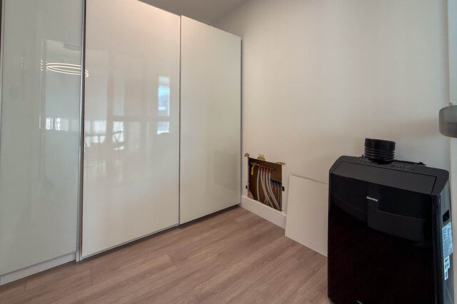 Bedroom with glossy white sliding closet doors, light wood-look flooring, and a black mini-fridge. - 1101-1067 Marinaside Crescent, Vancouver Downtown