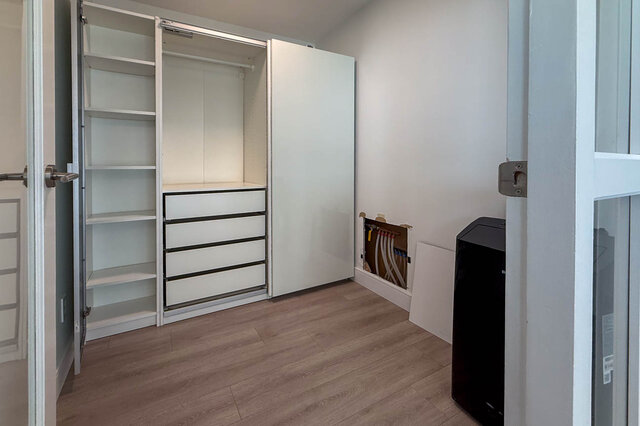Compact laundry room with light wood-look floors, a white sliding-door closet, and built-in drawers.