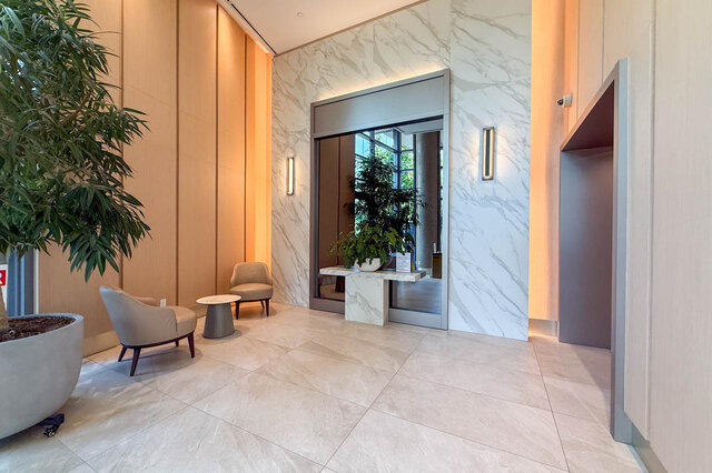 Elegant lobby entryway with a white marble feature wall, glass door, and two beige armchairs beside a potted plant.