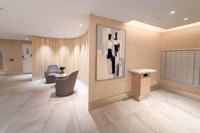 Spacious condo lobby with curved wood-slat wall, gray lounge chairs, and a large abstract artwork. - 1101-1067 Marinaside Crescent, Vancouver Downtown