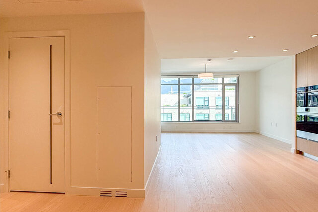 Open living space with light hardwood floors and a large window framing a mountain and city view. - 607-777 Harbour Way, North Vancouver