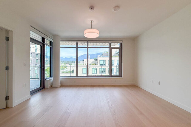 Spacious living room with light hardwood floors and large windows framing a mountain view. - 607-777 Harbour Way, North Vancouver