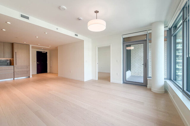 Spacious living room with light hardwood floors, a drum pendant light, and large windows opening to a balcony. - 607-777 Harbour Way, North Vancouver