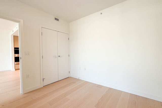 Empty den with light hardwood floors and white double doors, adjacent to a wood-cabinet nook. - 607-777 Harbour Way, North Vancouver
