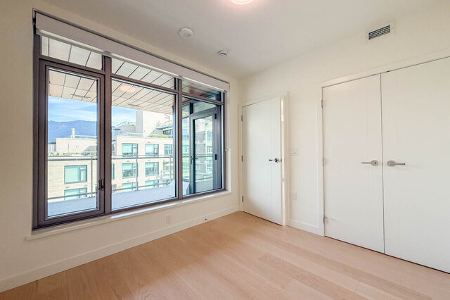 Bright bedroom with light hardwood floors and a large window framing a mountain and city view. - 607-777 Harbour Way, North Vancouver