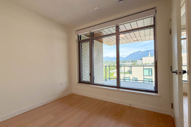 Bright bedroom with light hardwood floors and a large window framing a mountain view. - 607-777 Harbour Way, North Vancouver