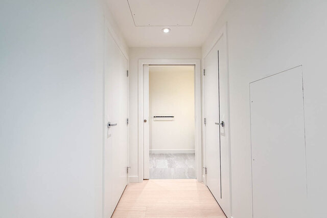 Bright hallway with light wood flooring and white doors leading to a tiled bathroom. - 607-777 Harbour Way, North Vancouver