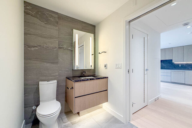 Modern powder room with floating wood vanity, dark granite countertop, and gray stone accent wall. - 607-777 Harbour Way, North Vancouver