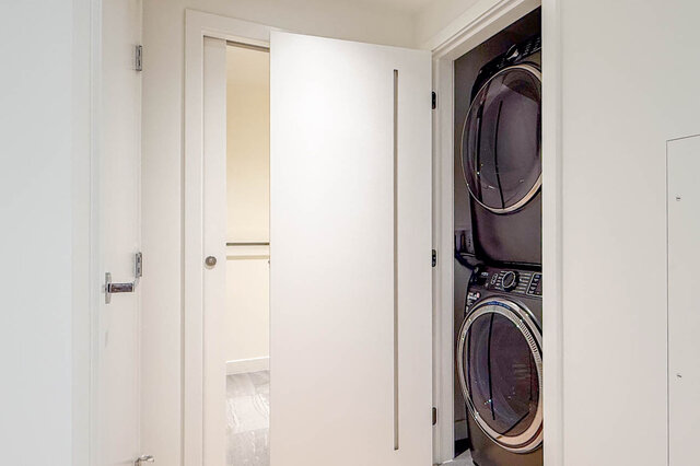 Laundry room with stacked washer and dryer beside a white door and closet with hanging rod. - 607-777 Harbour Way, North Vancouver