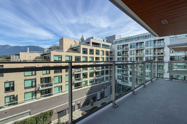 Spacious balcony with glass railing, wood ceiling, and distant mountain view. - 607-777 Harbour Way, North Vancouver