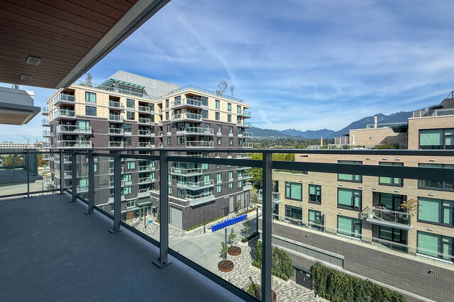 Spacious balcony with glass railing and wood-slat ceiling overlooking a courtyard and distant mountains. - 607-777 Harbour Way, North Vancouver