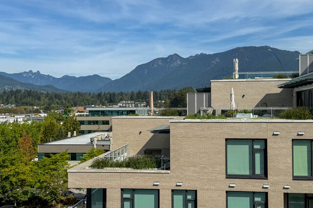 Rooftop terrace with brick facades and a sweeping view of forested North Vancouver mountains. - 607-777 Harbour Way, North Vancouver